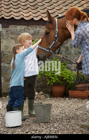Mutter und Kinder (5-6, 7-9) streicheln Pferd außen stabil Stockfoto