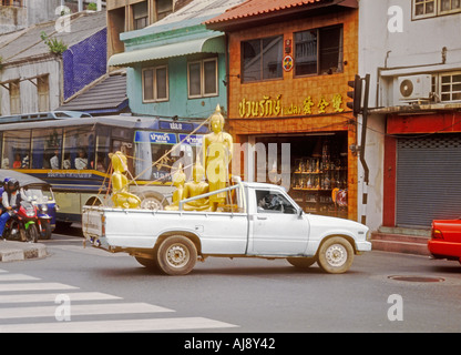 Weißer Pickup Truck Fahrer rauchen Zigarette Transport vier goldene stehender und sitzender Buddha Statuen durch Bamrung Muang in Bangkok, Thailand Stockfoto
