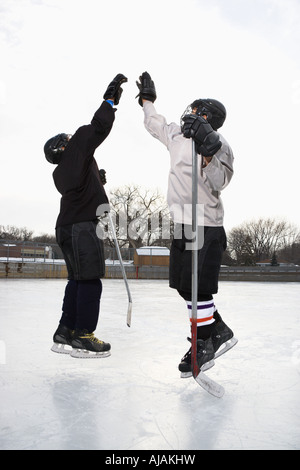 Zwei jungen im Eishockey Uniformen geben einander hoch fünf auf Eisbahn Stockfoto