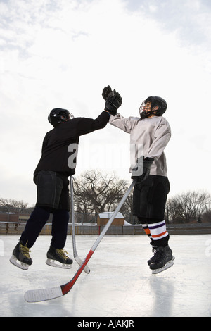 Zwei jungen im Eishockey Uniformen geben einander hoch fünf auf Eisbahn Stockfoto