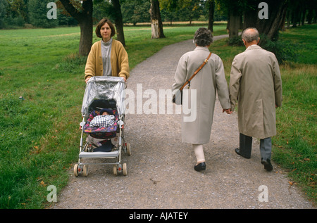 Eine junge und einsame Mutter schiebt ihren Kinderwagen s vorbei an ein älteres Ehepaar in einem Park in London England Stockfoto