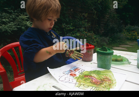 Ein junges Kindes Mädchen malt ihre eigene Hand rot, als sie mit Wasserfarben in ihrem Garten hinter dem Haus London spielt Stockfoto