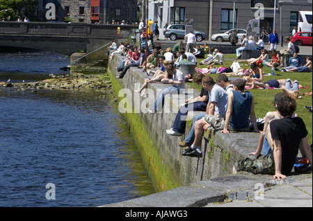 Menschen genießen die Sonne am Kai neben dem Fluss Corrib an einem Sonntag Nachmittag Stockfoto