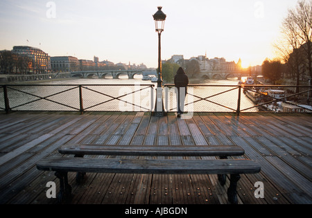 Ein einsamer Kapuzengestalt steht suchen gefährdeten während gebeugt über Geländer auf der Seine auf der Pont des Arts Paris Stockfoto