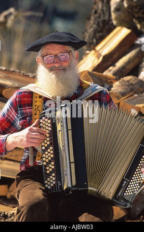 bärtige Daryman spielt Bandoneon, tragen Mütze und Brille, sitzen vor Holzstapel Stockfoto