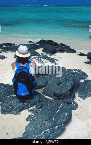 Frau mit Rucksack sitzt am Strand, Hut, Blick auf Meer Stockfoto