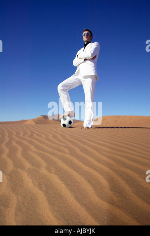 Mann in einem weißen Anzug, stehend auf einem Fußball in der Wüste Stockfoto