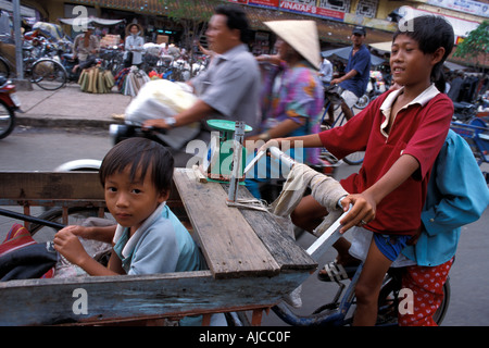 Vietnamesische jungen fahren eine Markt-Rikscha mit jüngeren Bruder vor anstrengenden Ho Chi Minh Stadt Saigon street Stockfoto