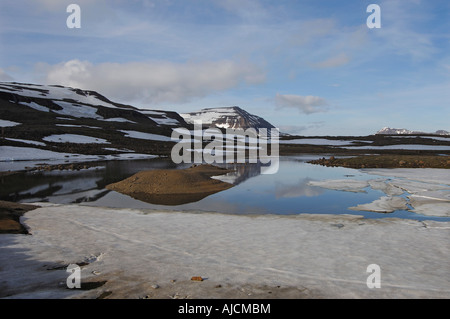 Teilweise noch gefroren Schmelzwasser Pool und den Berg Bjolfur im Bereich von Fjardarheidi in der Nähe von Seydisfjordur East Island Stockfoto