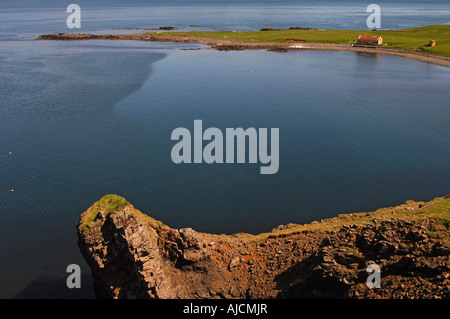 Schroffe Felsen oben und alte Wirtschaftsgebäude am Ufer des Reydarfjördur in der Nähe von Vattarnes im Osten Fjorde Osten Islands Stockfoto