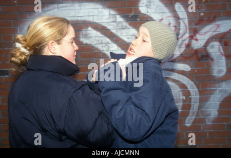 ein junges Mädchen treibt einen jüngeren Jungen gegen eine Wand, die ihn Würgen Stockfoto