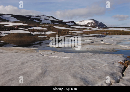 Teilweise noch gefroren Schmelzwasser Pool und den Berg Bjolfur im Bereich von Fjardarheidi in der Nähe von Seydisfjordur East Island Stockfoto