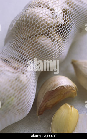 Nahaufnahme des Netzes mit Knoblauchzwiebeln und einigen Nelken auf einem Schneidebrett. Stockfoto