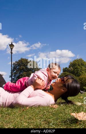 Asiatische Mutter und Mischlinge vier Monate altes Baby spielt gerne in einem Londoner Park mit blauem Himmel und weißen Wolken; Verklebung & Liebe Stockfoto