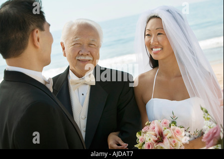 Braut und Vater Arm in Arm mit Bräutigam bei der Hochzeit am Strand Stockfoto