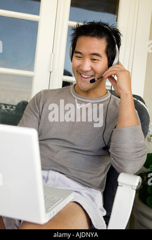 Mann trägt Kopfhörer mit Laptop auf der Veranda Stockfoto