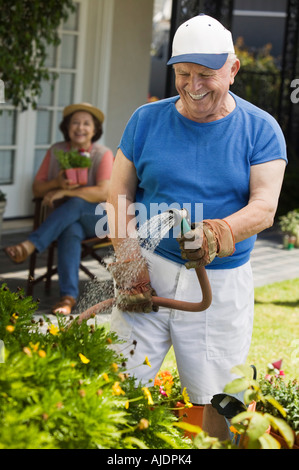 Senior woman Bewässerung von Pflanzen im Garten, Frau im Hintergrund Stockfoto