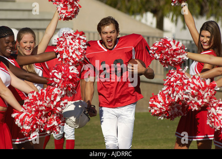 Football-Spieler zwischen Cheerleadern auf Feld Stockfoto