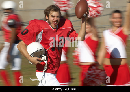Fußballspieler mit Ball laufen von Cheerleadern Stockfoto