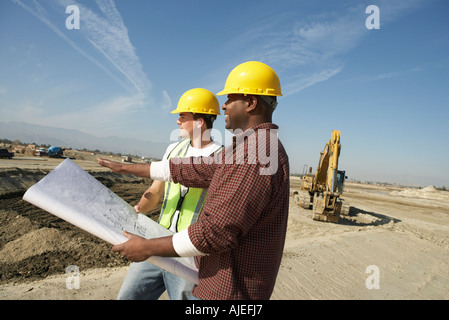 Bauarbeiter tragen Schutzhelme, Blick auf Plan vor Ort Stockfoto