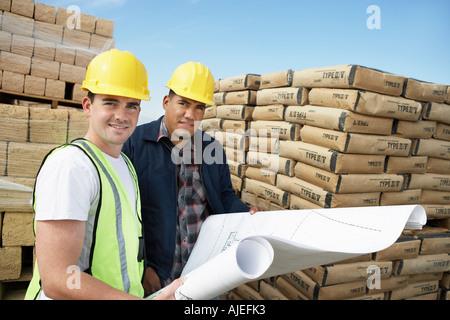 Bauarbeiter in der Nähe von Lieferungen stehen, tragen Schutzhelme, Blick auf Plan vor Ort Stockfoto