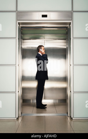 Geschäftsmann mittels Handy im Aufzug, Seitenansicht Stockfoto