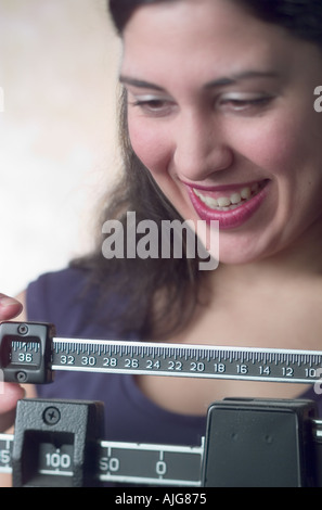 Kaukasische junge Frau angenehm überrascht, wenn Sie ihr Gewicht auf die Waage überprüft Stockfoto