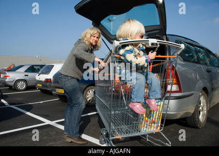 Foto von einer Mutter und ihre zwei Jahre alte Tochter die wöchentlichen Einkäufe ins Auto laden Stockfoto