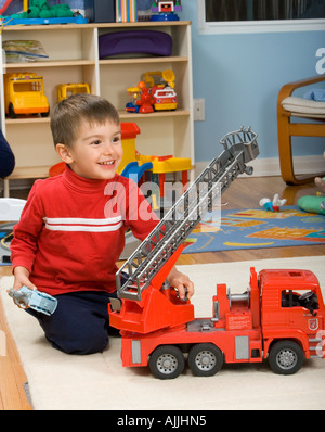 drei Jahre alte Junge spielt mit großen Feuerwehrauto im Schlafzimmer Stockfoto