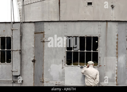 Alte Mann trägt eine flache Kappe, Blick auf den internen Mechanismus des Dock Kran durch das Fenster Stockfoto