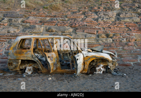 Rostige ausgebrannte Auto Schale am Strand mit stonewall im Hintergrund uk Stockfoto