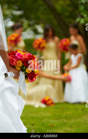 der Hochzeitstag - Brautjungfern und Flowergirls in Ferne zu sehen, während eine Braut im Vordergrund ihr Strauß Rosen hält Stockfoto