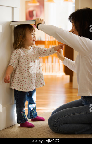 Measing asiatische Mutter ihre kleine Tochter Höhe gegen eine Tür zu Hause Stockfoto