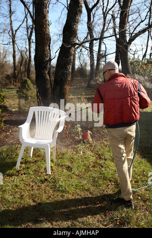 Rückseite ein Mann macht waschen weißen Plastikstuhl auf dem Rasen mit Bäumen und Wald im Hintergrund. Stockfoto
