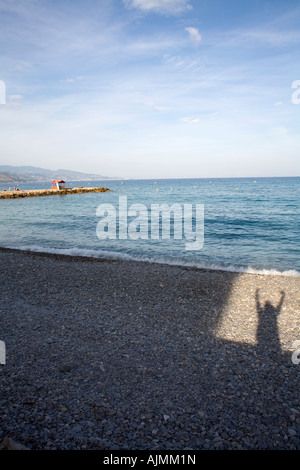 Schatten springen Person auf einem Kiesstrand mit einem mediterranen Horizont. Sieger des Rennens, überglücklich. Sprung aus einer box Stockfoto