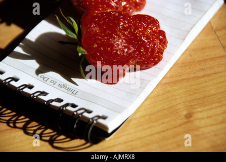 zwei Erdbeeren frisch gepflückt und ruht auf einem Notizblock im Sonnenschein Stockfoto