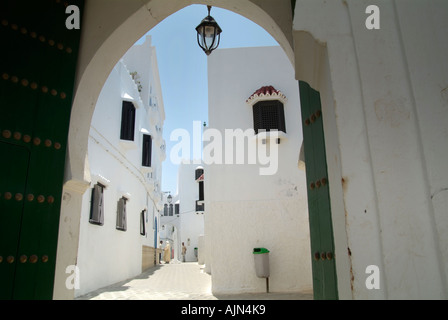 Der Blick durch einen Torbogen einer Straße mit gepflegten weiß getünchten traditionellen Gebäuden in der Altstadt von Asilah. Stockfoto