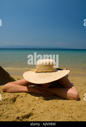 Frau Frau Stroh Hut liegen am Sandstrand mit blauen Mittelmeer und Himmel im Hintergrund Stockfoto