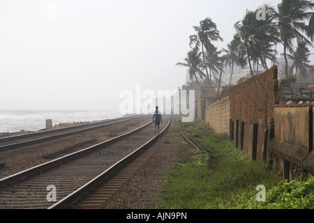 Eine Person geht entlang der Bahnlinie, die direkt am Strand entlang und in die Hauptstadt von Sri Lanka, Colombo ausgeführt wird. Stockfoto