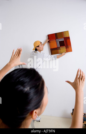 Rückansicht einer Frau helfen, einen jungen Mann ein Gemälde an der Wand anpassen Stockfoto