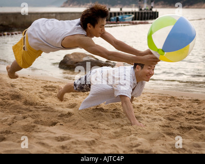 Zwei junge Männer am Strand mit einem Wasserball spielen Stockfoto