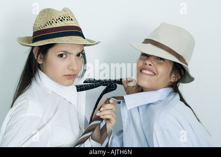 Zwei junge Freundinnen mit Button-down Hemden, Krawatten und Hüte bekleidet, ziehen am jeweils anderen Bindungen, Porträt Stockfoto