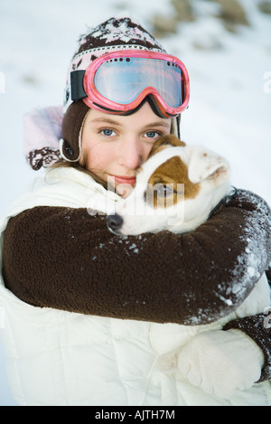 Teenager-Mädchen umarmt Hund, gekleidet in Winterkleidung, lächelnd in die Kamera, Porträt Stockfoto