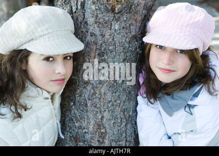 Zwei junge Freunde gelehnt Baumstamm, beide tragen Mützen, lächelnd in die Kamera, Porträt Stockfoto