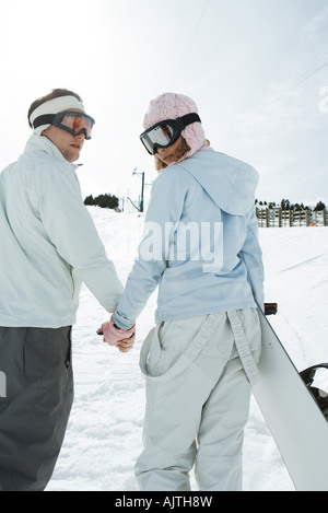 Zwei junge Freunde gehen, Hand in Hand, Blick über die Schultern, eine Tragetasche Snowboard, Rückansicht Stockfoto