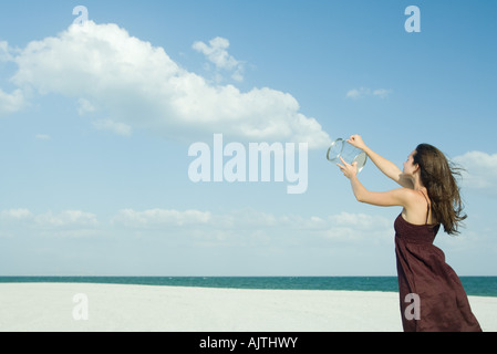 Frau am Strand stehen, hält klare Container, Freigabe von Wolken, optische Täuschung Stockfoto