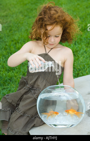 Rothaarige Mädchen gießt Wasser in Flaschen in Goldfischglas Stockfoto