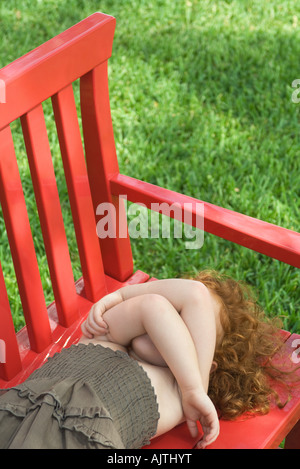 Kleines Mädchen auf rote Bank im Schatten, grünen Rasen im Hintergrund, erhöhte Ansicht, Taille oben liegend Stockfoto