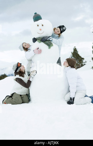 Junge Freundinnen gruppieren sich um Schneemann Stockfoto