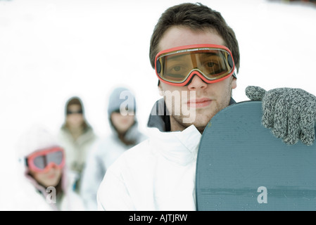 Junge männliche Snowboarder Blick in die Kamera, Freunde stehen im Hintergrund, Porträt Stockfoto